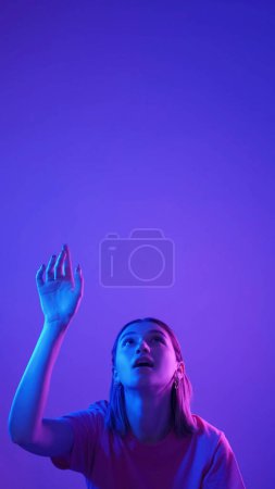 Foto de Clic virtual. Elegir alta tecnología. Luz de color neón sorprendida chica excitada alcanzando dedo presionando la opción de selección aislado en azul rosa vacío espacio de fondo. - Imagen libre de derechos