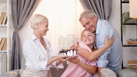 Téléchargez les photos : Gâteau d'anniversaire. Fête de famille. Fête de vacances. Homme excité embrassant fille lorsque la mère tenant pâtisserie festive à l'intérieur de la maison lumière. - en image libre de droit