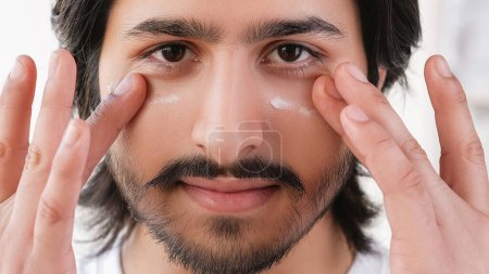 Photo for Male cleansing cream. Skin care. Attractive confident man with beard mustache applying moisturizer on face cosmetic procedures in light room. - Royalty Free Image