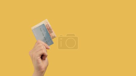 Photo for Cashless transfer. Financial profit. Woman hand showing rubles and credit card on yellow background copy space. - Royalty Free Image