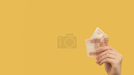Téléchargez les photos : Revenus passifs. Un geste d'argent. Main féminine tenant roubles russes 500 sur fond jaune espace de copie. - en image libre de droit