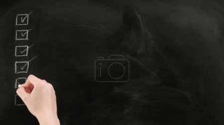 Photo for Checkbox list. Done sign. Woman hand marking off tasks with tick on black chalkboard copy space. - Royalty Free Image