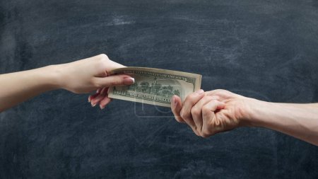 Photo for Money gestures. Family finances. Husband hand giving to wife salary in dollars on black chalkboard. - Royalty Free Image
