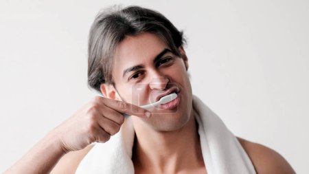 Téléchargez les photos : Je me brosse les dents. Santé dentaire. La routine orale. gars attrayant serviette blanche sur les épaules hygiène du matin isolé sur fond blanc espace de copie. - en image libre de droit