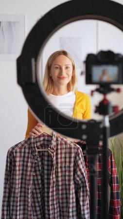 Fashion influencer. Stylist vlogging. Satisfied happy woman recording video blog showing trendy outfit new season filming camera tripod ring light in home interior.
