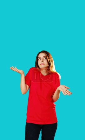 Photo for Whatever gesture. Clueless woman. Who knows. Indifferent girl in red T-shirt shrugging shoulders isolated on cyan blue empty space background. - Royalty Free Image
