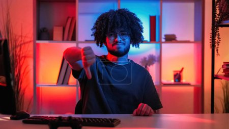 Photo for Refusing man. Hand expression. Negative answer. Hipster guy showing dislike gesture sitting work desk in dark neon light room interior. - Royalty Free Image