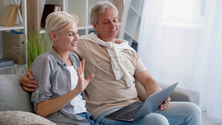 Photo for Online meeting. Happy couple. Digital connection. Smiling middle-aged man and woman having video call on laptop sitting light home interior. - Royalty Free Image