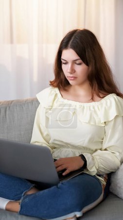 Photo for Freelance work. Online job. Internet communication. Focused young woman sitting on sofa crossed legs with laptop typing on keyboard at home. - Royalty Free Image