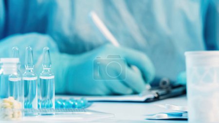Photo for Doctor prescription. Medical paperwork. Physician hand in protective rubber gloves writing on clipboard. Tablets bottle blisters and ampules on white table. - Royalty Free Image