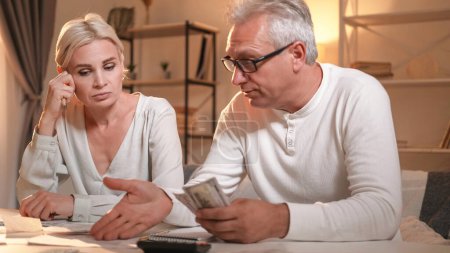 Photo for Family payment. Debt problems. Pensive man woman arranging money planning budget counting bills couple financial troubles sitting table in light shadow room interior. - Royalty Free Image
