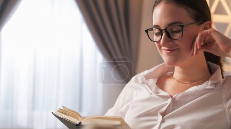 Photo for Book lover. Learning hobby. Study leisure. Relaxed happy smart intelligent woman in glasses enjoying reading novel at light home interior with free space. - Royalty Free Image