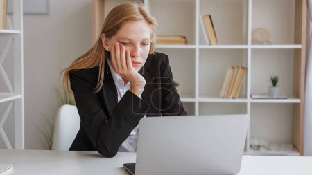 Photo for Work burnout. Professional frustration. Exhausted young woman in business jacket sitting chin on hand before laptop with tired look at office. - Royalty Free Image