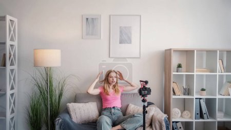 Photo for Vlog content. Video tutorial. Expressive young freelance blond woman talking sharing skills to camera on tripod with hands up in white interior at home free space. - Royalty Free Image
