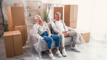 Photo for Moving house. New home. Tired unhappy couple man woman feeling fatigue relocating in apartment with many boxes sitting sofa light room interior. - Royalty Free Image
