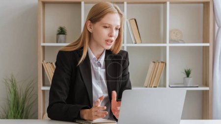 Photo for Video conference. Conversation online. Virtual communication. Confident woman sitting at table in business suit speaking to laptop gesticulating. - Royalty Free Image