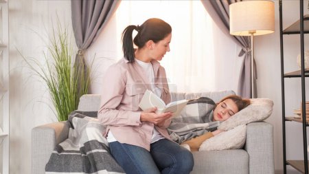 Photo for Family reading. Parent leisure. Loving mother declaiming interesting story from book to napping teenager girl laying sofa light room interior. - Royalty Free Image