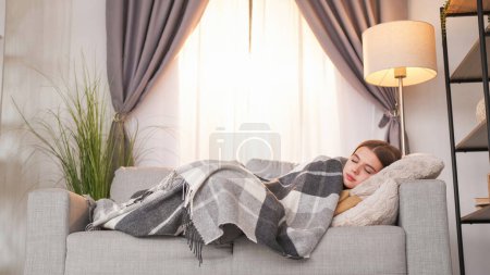 Foto de Relajación. Sofá de descanso. Siesta de día. Chica satisfecha durmiendo debajo de la manta en un cómodo sofá disfrutando del descanso en fin de semana daydream en el interior de la habitación de luz. - Imagen libre de derechos