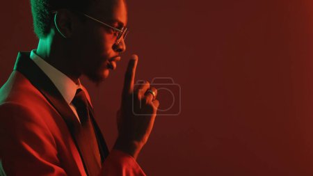 Photo for Man hush. Secret conspiracy. Neon light profile of gentleman in elegant tuxedo suit glasses finger ring warning with shh gesture on dark red empty space background. - Royalty Free Image