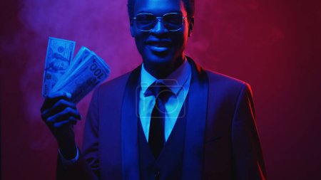 Photo for Millionaire cash. Lottery winner. Financial reward. Pink blue neon light satisfied smiling rich business man in suit showing 100 US dollar money fan in color smoke on dark. - Royalty Free Image