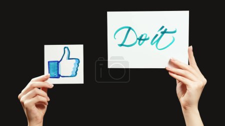 Photo for Kharkiv, Ukraine - May 12, 2020: Do it like. Support motivation. Social media approval. Female hands showing encouraging message thumb up sign isolated on black free space. - Royalty Free Image