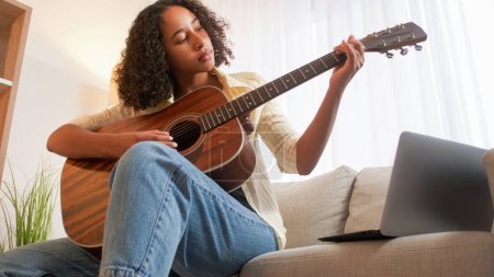 Photo for Guitar hobby. Music practice. Weekend leisure. Focused woman playing chords on acoustic string instrument sitting sofa at home room. - Royalty Free Image