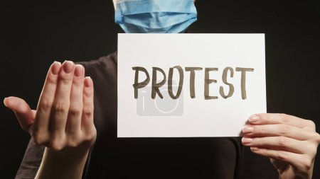 Photo for Join protest. Pandemic demonstration. Unrecognizable female activist in face mask inviting for strike with hand gesture placard sign on black. - Royalty Free Image