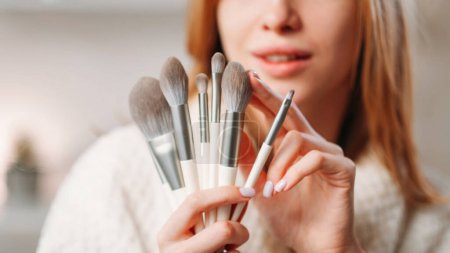 Photo for Makeup brushes. Visage tools. Beauty accessories. Unrecognizable woman hands holding testing eyeshadow powder blusher cosmetic applicators set collection for face skin on copy space. - Royalty Free Image