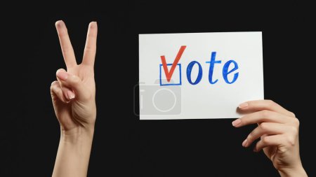 Photo for Vote approval. Election victory. Female hand supporting decision with peace V sign gesture check mark bulletin isolated on dark black free space. - Royalty Free Image