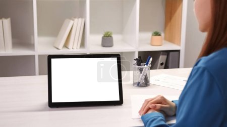 Foto de Reunión virtual. Videoconferencia. Mujer en la tableta con espacio vacío pantalla de maqueta blanca trabajando en el proyecto en la llamada de negocios en el escritorio del lugar de trabajo de oficina. - Imagen libre de derechos