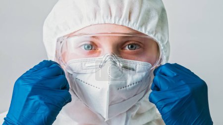 Photo for Air contamination. Ecological disaster. Respiratory protection. Woman scientist in blue gloves putting on equipment white face mask goggles isolated on grey background. - Royalty Free Image