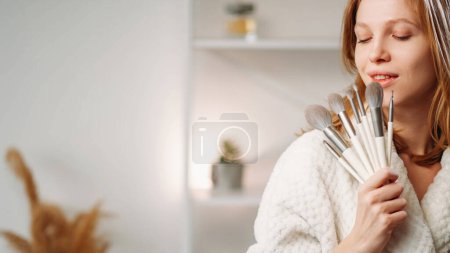 Photo for Makeup brushes. Cosmetic tools. Morning visage. Satisfied woman with radiant face skin holding eyeshadow powder blusher applicators set collection in light interior with free space. - Royalty Free Image