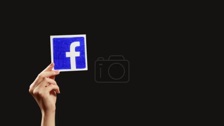Photo for Kharkiv, Ukraine - May 12, 2020: Follow Facebook. Global communication. Female hand showing social network app logo isolated on dark black empty space background. - Royalty Free Image