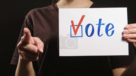 Wählen Sie. Politischer Wahlkampf. Bürgerliche Verantwortung. Unerkennbare Frauenhand, die sich aufregt, um einen Kandidaten zu wählen, der mit dem Zeigefinger auf dem dunklen Kopierraum mit dem Häkchen auf dem Stimmzettel zeigt.