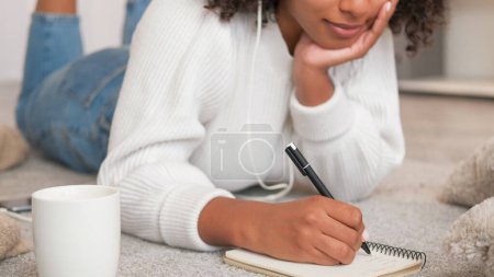Photo for Diary planning. Journal handwriting. Personal list. Closeup of unrecognizable woman writing notes in notebook enjoying home leisure on cozy floor. - Royalty Free Image