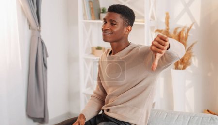 Photo for Disapproval gesture. Negative opinion. Disappointed man with thumbs down sign unhappy about expensive home rent living room interior. - Royalty Free Image
