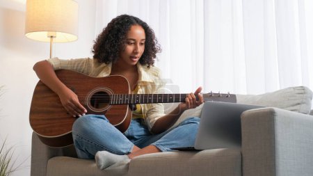 Foto de Escuela en línea. Clase de guitarra. Aprendizaje remoto. Mujer guitarrista practicando instrumento de cuerda clase de internet en el sofá sentado portátil en la habitación de casa. - Imagen libre de derechos