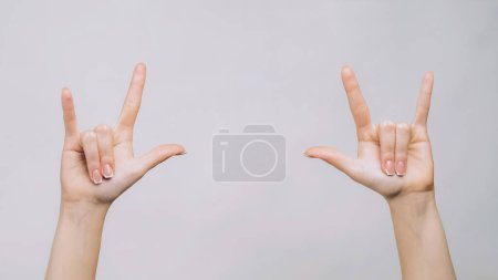 Téléchargez les photos : Panneau rock. Un geste pourri. doigts de femme montrant des cornes symboles isolés sur fond d'espace libre gris. - en image libre de droit