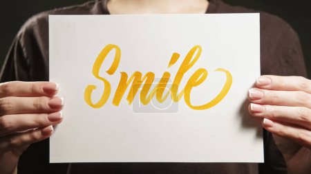 Photo for Smile sign. Positive motivation. Encouraging message. Unrecognizable woman supporting with optimistic support word text placard in hands. - Royalty Free Image