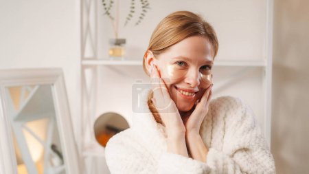 Photo for Hydrogel patches. Skincare beauty. Facial moisturizing cosmetology. Happy woman enjoying touching clean face skin with golden under eye gel pads in light interior with copy space. - Royalty Free Image