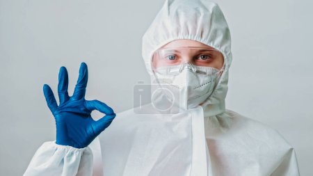 Photo for Healthcare worker. Coronavirus pandemic. Okay gesture. Female woman doctor in white protective coverall suit with well done hand sign isolated on grey background. - Royalty Free Image