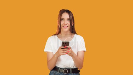 Photo for Smartphone chat. Messenger advertisement. Fun online communication. Happy pensive woman typing on cell isolated on orange background copy space. - Royalty Free Image