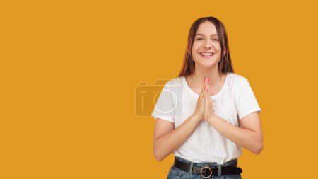 Téléchargez les photos : Un geste de vœux. Des mains de gratitude. Jeune femme souriante heureuse exprimant appréciation reconnaissante attitude reconnaissante isolé sur fond orange espace vide. - en image libre de droit
