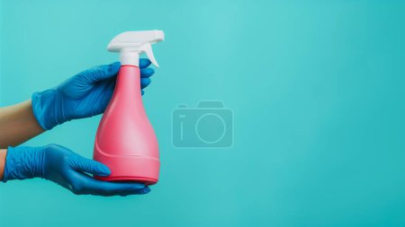 Téléchargez les photos : Spray désinfectant. Nettoyage efficace. Mains de femme au foyer dans des gants de protection en latex démontrant bouteille rose isolé sur fond vert espace vide. - en image libre de droit