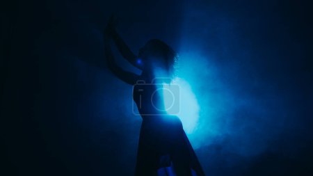 Foto de Rendimiento corporal. Coreografía de silueta. apasionada emocional hermosa mujer bailando en azul vapor punto luz sobre fondo oscuro copia espacio. - Imagen libre de derechos