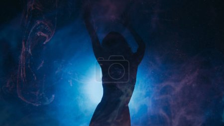 Photo for Spiritual dance. Ethereal energy. Emotional passionate woman silhouette moving in haze shadow neon spot light dark blue magic background copy space. - Royalty Free Image