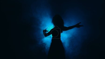 Photo for Silhouette dancing. Contemporary performance. Graceful flexibility. Tender slim woman moving in haze shadow spot light dark background copy space. - Royalty Free Image