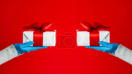 Photo for Festive present. Epidemic gifts. Unrecognizable human hands in rubber gloves holding wrapped boxes coronavirus protective gear isolated on red free space background. - Royalty Free Image