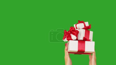 Foto de Entrega de regalos. Bono navideño. Manos de mujer irreconocibles sosteniendo cajas envueltas regalos festivos aislados en el fondo de espacio de copia verde. - Imagen libre de derechos