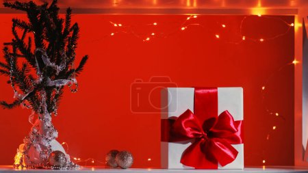 Photo for Christmas celebration. Winter holidays decoration. New Year party organization. Gift box with embellished fir tree branch balls fairy lights isolated on red copy space background. - Royalty Free Image